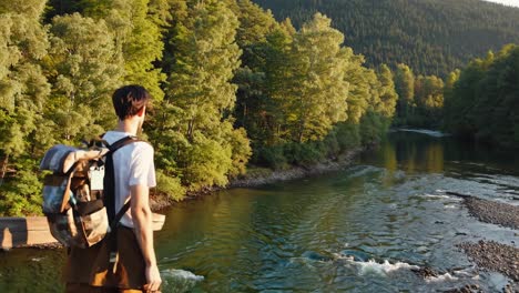 aerial video shot of a hiker with a backpack overlooking a serene river surrounded by forest video