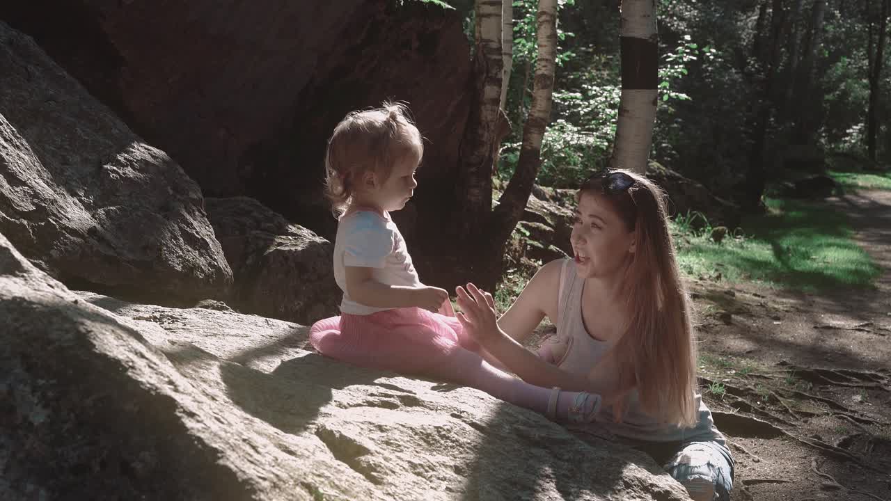 madre y hija hermosas hablando en un bosque cerca de una piedra grande