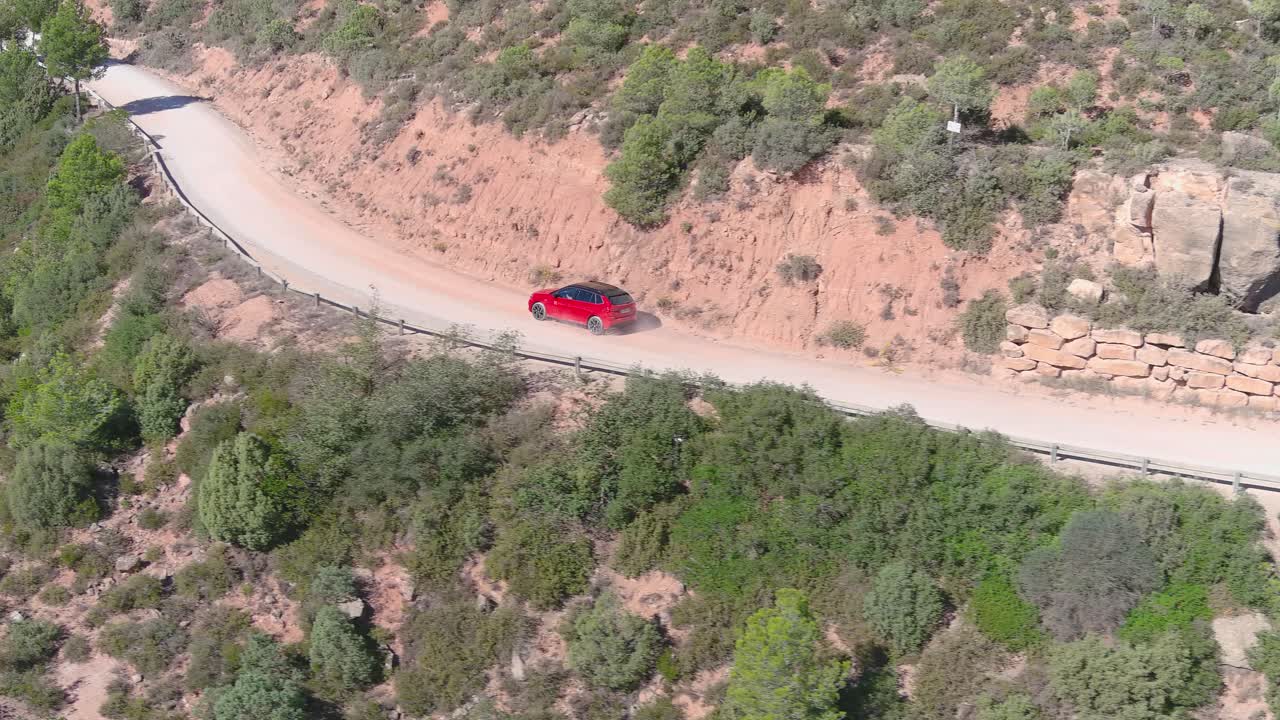 vista aérea de un coche rojo conduciendo a través de las montañas en una carretera rural