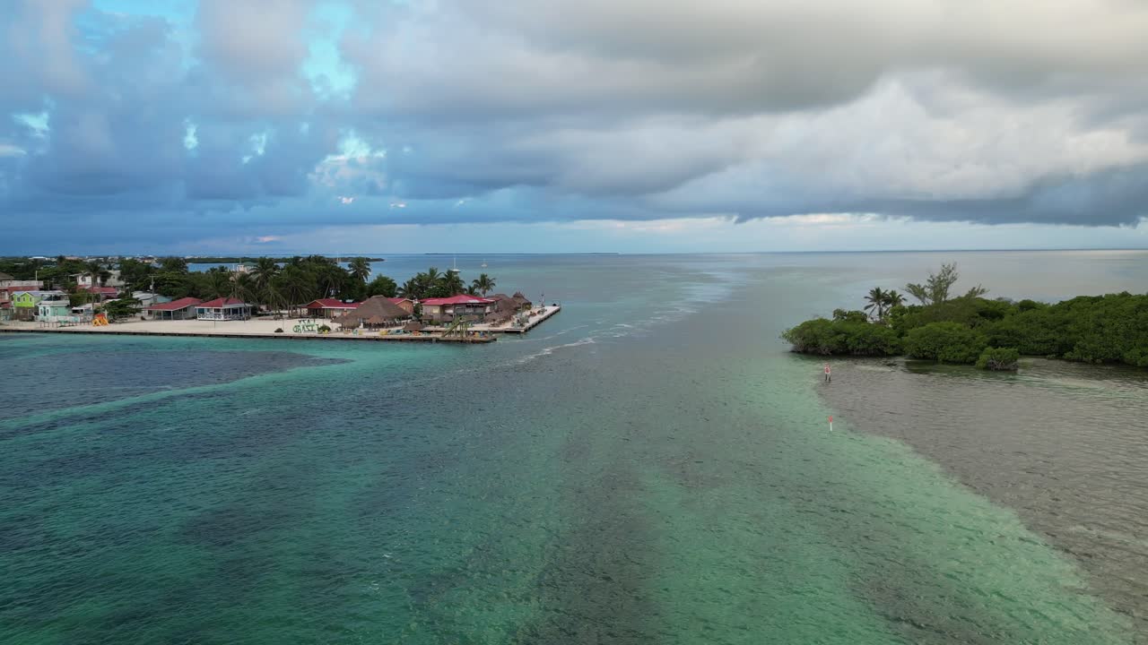 vista de avión no tripulado en belice volando sobre el mar azul oscuro y claro del caribe, un cay de arena blanca cubierto de palmeras y restaurantes en un día nublado