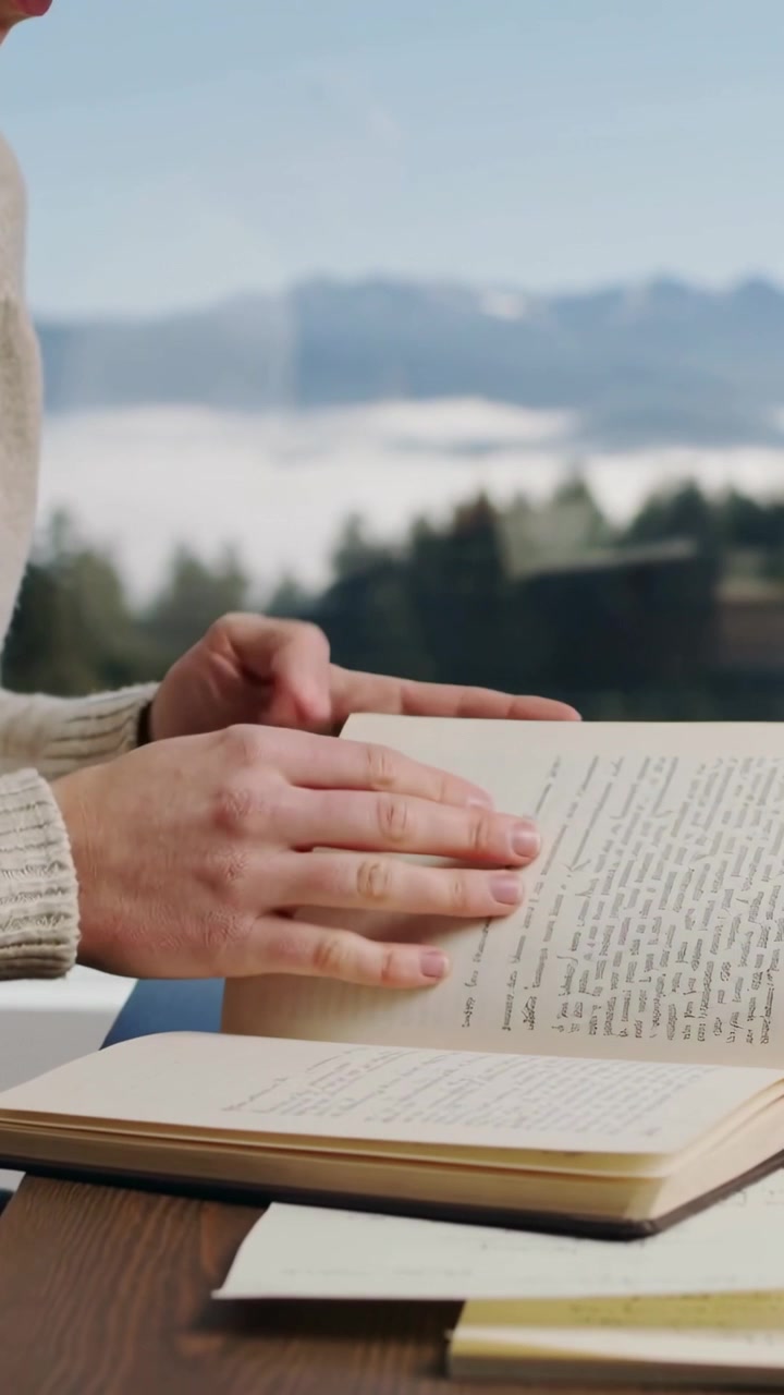 Vertical video: Resting hand on book, woman in sweater turning pages, reading by window, copy space