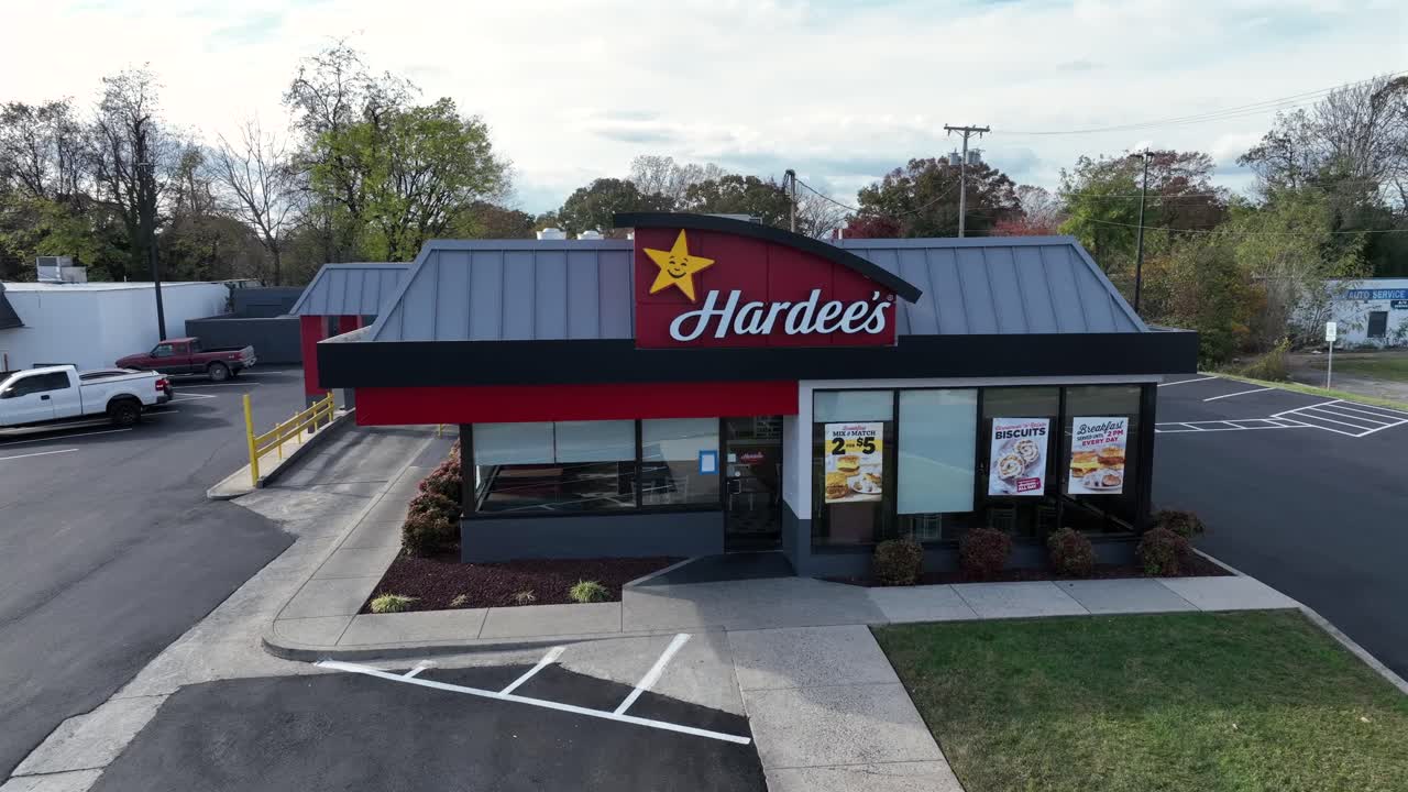 Aerial approaching shot of Hardees Restaurant on american city. Sunny day in autumn Season. Parking cars on lot. Star Sigh and advertisement in window.