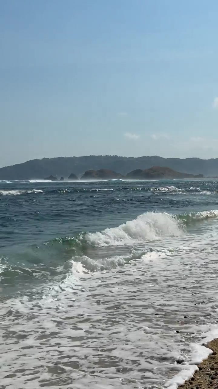 Onde dell'oceano che si infrangono su una spiaggia sabbiosa con colline lontane