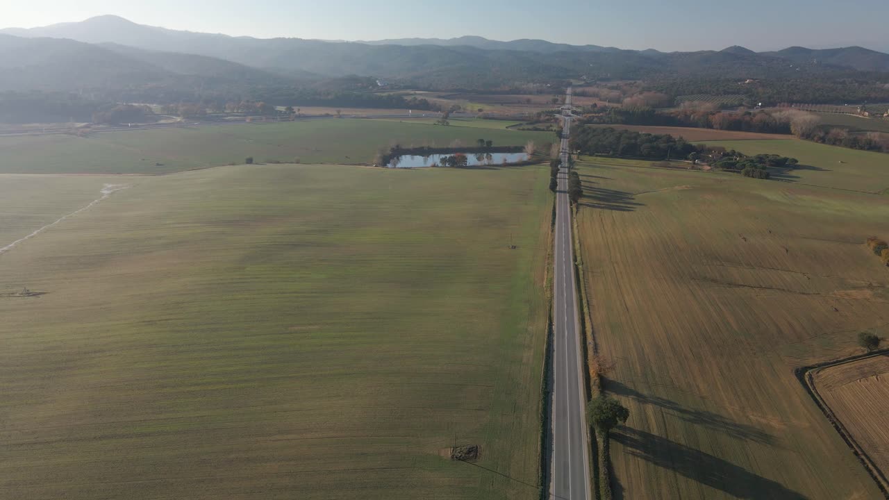 Aerial video of a newly seeded field with a dirt road in the middle and mountains in the background green Llagostera Gerona cultivated field