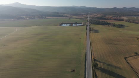 Luftvideo-Eines-Neu-Gesäten-Feldes-Mit-Einer-Unbefestigten-Straße-In-Der-Mitte-Und-Bergen-Im-Hintergrund-Grünes-Kultiviertes-Feld-Von-Llagostera-Gerona