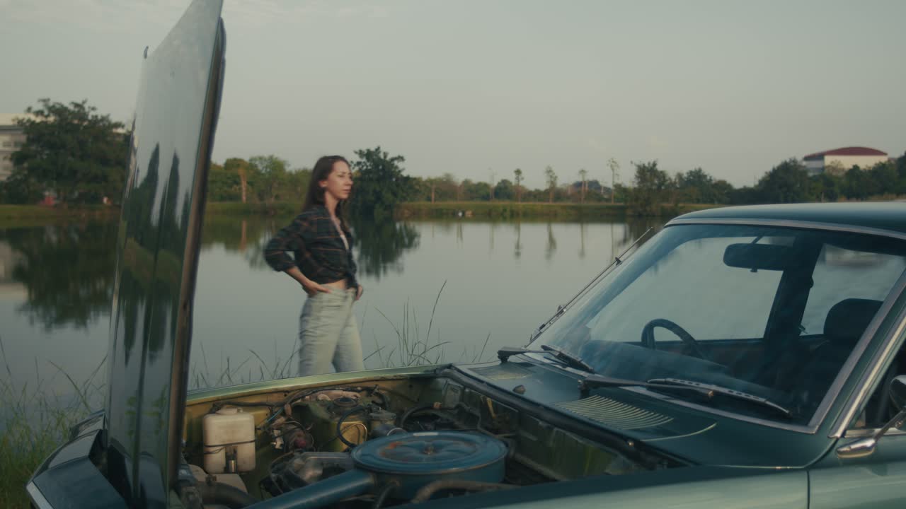 Woman repairing a vintage car by the lake