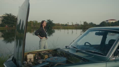 woman repairing a vintage car by the lake