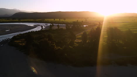 Eine-Atemberaubende-Aussicht-über-Den-Grünen-Feldern,-Palmen-Und-Einem-Fluss-In-Hokitika,-Mit-Sonnenuntergang-Im-Hintergrund,-Neuseeland