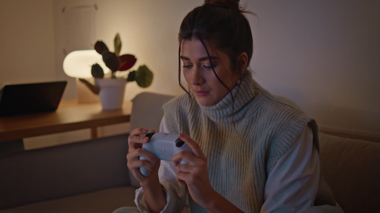 Primo piano: giocatrice concentrata con controller di gioco a casa di notte. Donna che impugna il joystick