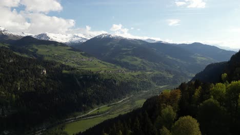 Una-Vista-Aérea-Contempla-El-Valle-De-Obersaxen,-Enclavado-En-El-Majestuoso-Abrazo-De-La-Cordillera-De-Los-Grisones,-Coronada-Por-Picos-Nevados.