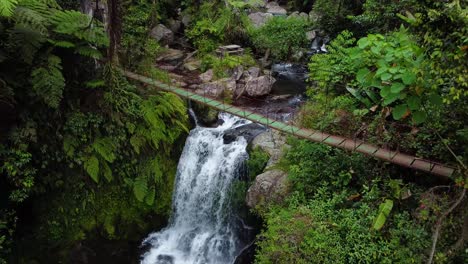 drone shot of a waterfalls passing a foot bridge