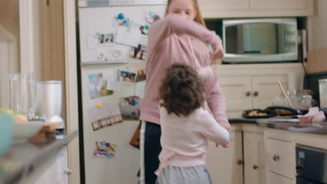 happy teenage girl dancing with little sister in kitchen siblings having fun enjoying funny dance at home together on weekend