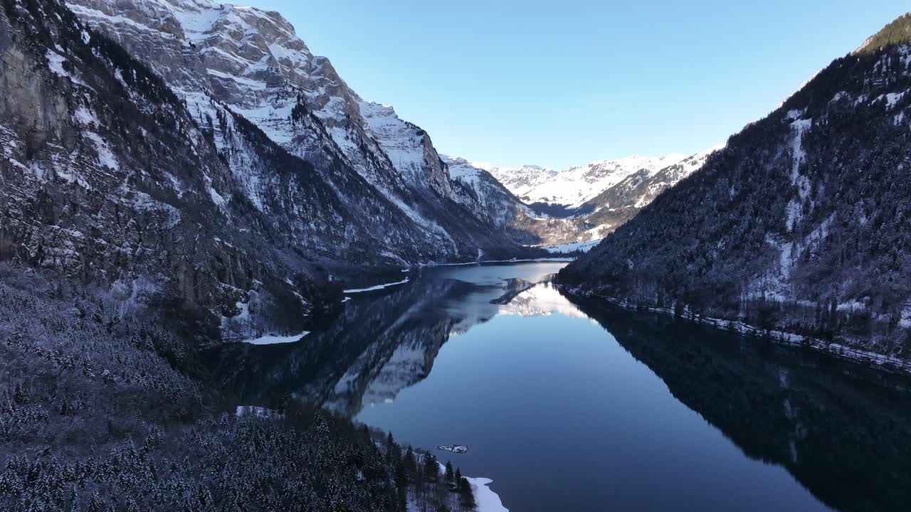 Aerial Klöntalersee reflecting snowy Alps in Klöntal, Switzerland, serene winter landscape