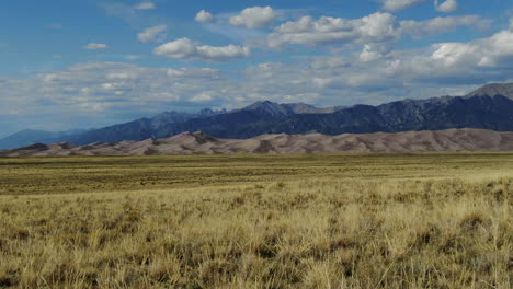 Aéreo-Cinemático-Dron-Paralaje-Vista-De-Apertura-De-Finales-De-Verano-Entrada-Del-Parque-Nacional-De-Las-Grandes-Dunas-De-Arena-Colorado-Montaña-Rocosa-14er-Picos-Crujiente-Amarillo-Dorado-Hierba-Alta-Cielo-Azul-Deslizarse-Hacia-La-Izquierda