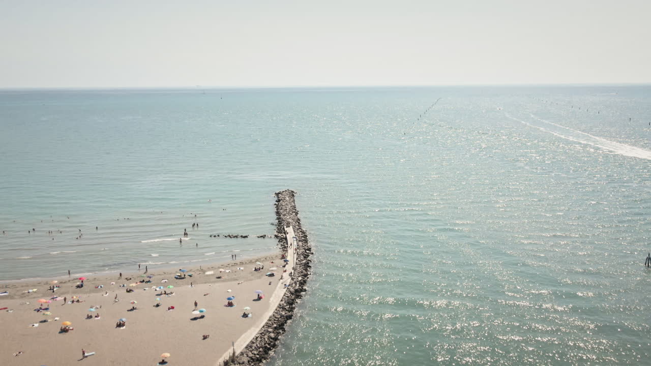 Drone 4K UHD yang mulus terbang maju di atas Laguna Grado menuju pantai berpasir dan area pemukiman pesisir—ideal untuk film perjalanan, rekaman pembuka