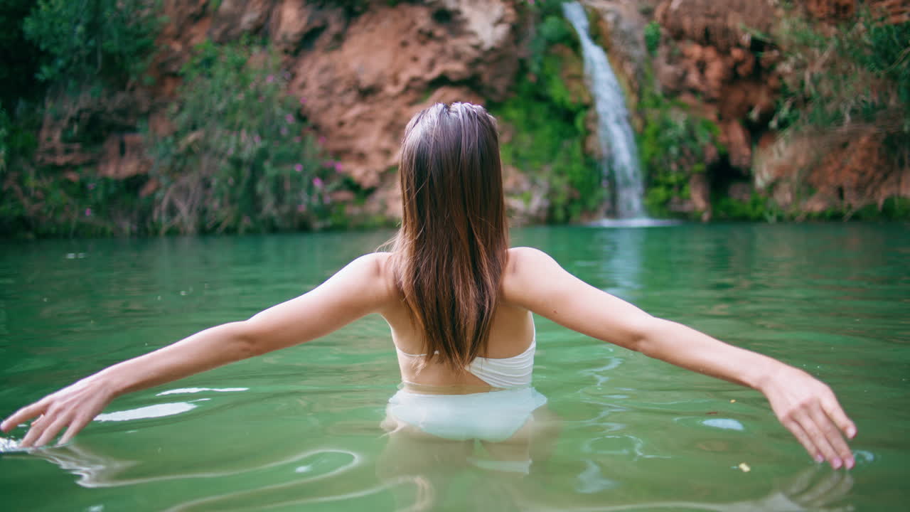레이디의 손이 호수 표면을 만지는 클로즈업.