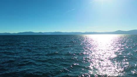 drone flying close above glistening waters of lake tahoe in california on a sunny day with mountains in the background