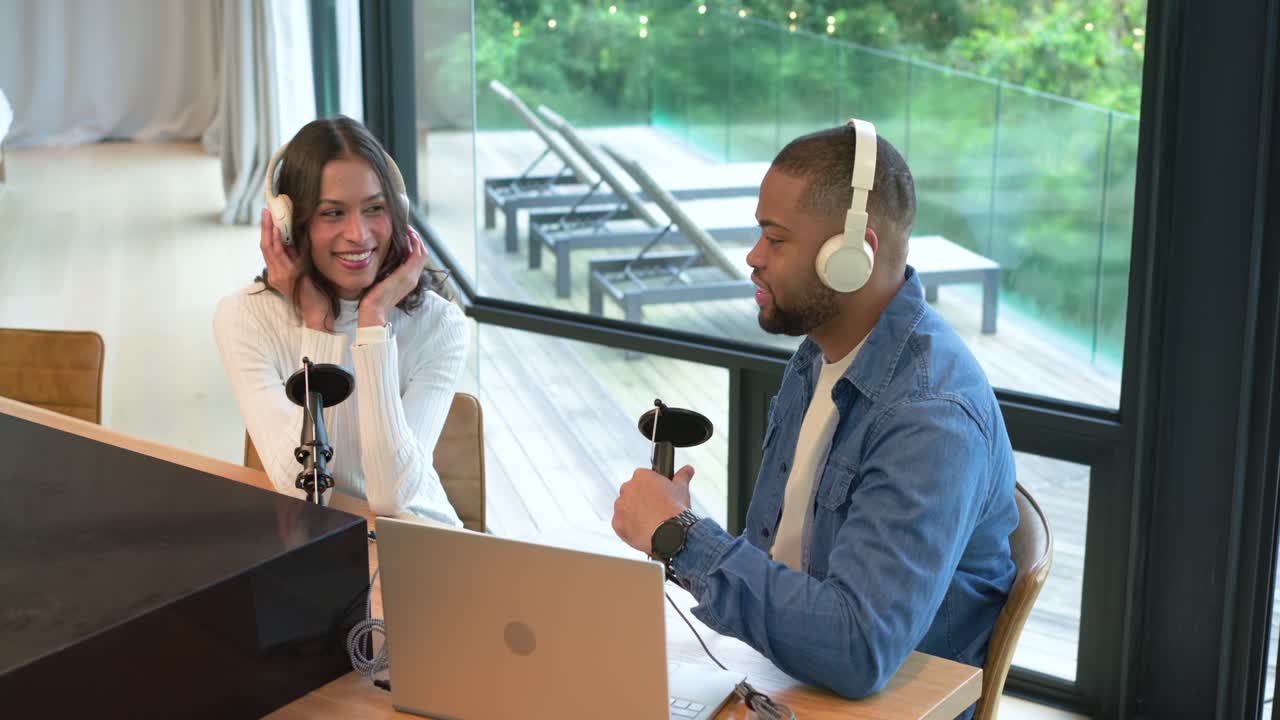 Podkastverter tar på seg hodetelefoner og justerer mikrofoner etter å ha skrevet på en bærbar datamaskin i studio