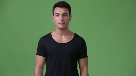 young handsome hispanic man against green background