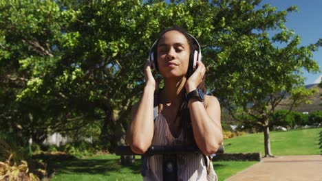 african american woman on scooter wearing headphones and listening to music in park