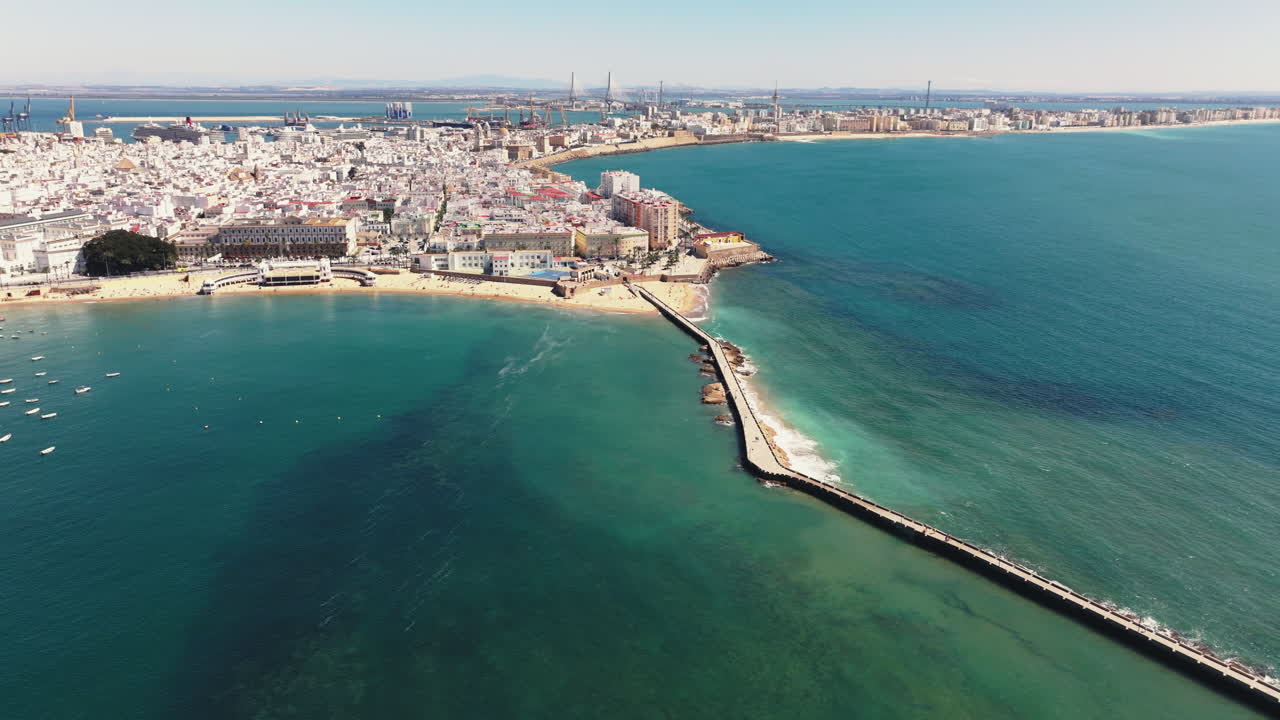 Vista aerea della città vecchia di Cadice e dell'area di La Caleta con frangiflutti e spiagge che si estendono nell'Oceano Atlantico, ripresa da un drone. Panorama della città sotto un cielo azzurro e limpido in Andalusia, Spagna, Europa. Color grading cinematografico