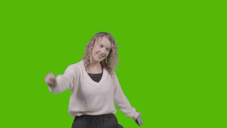 studio shot of young woman listening to music on mobile phone and dancing against green screen 4