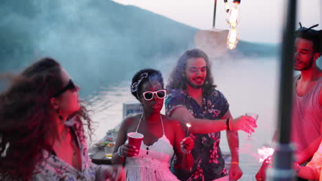 young friends dancing with sparklers at lake party