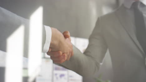 colleagues shaking hands behind glass wall in office