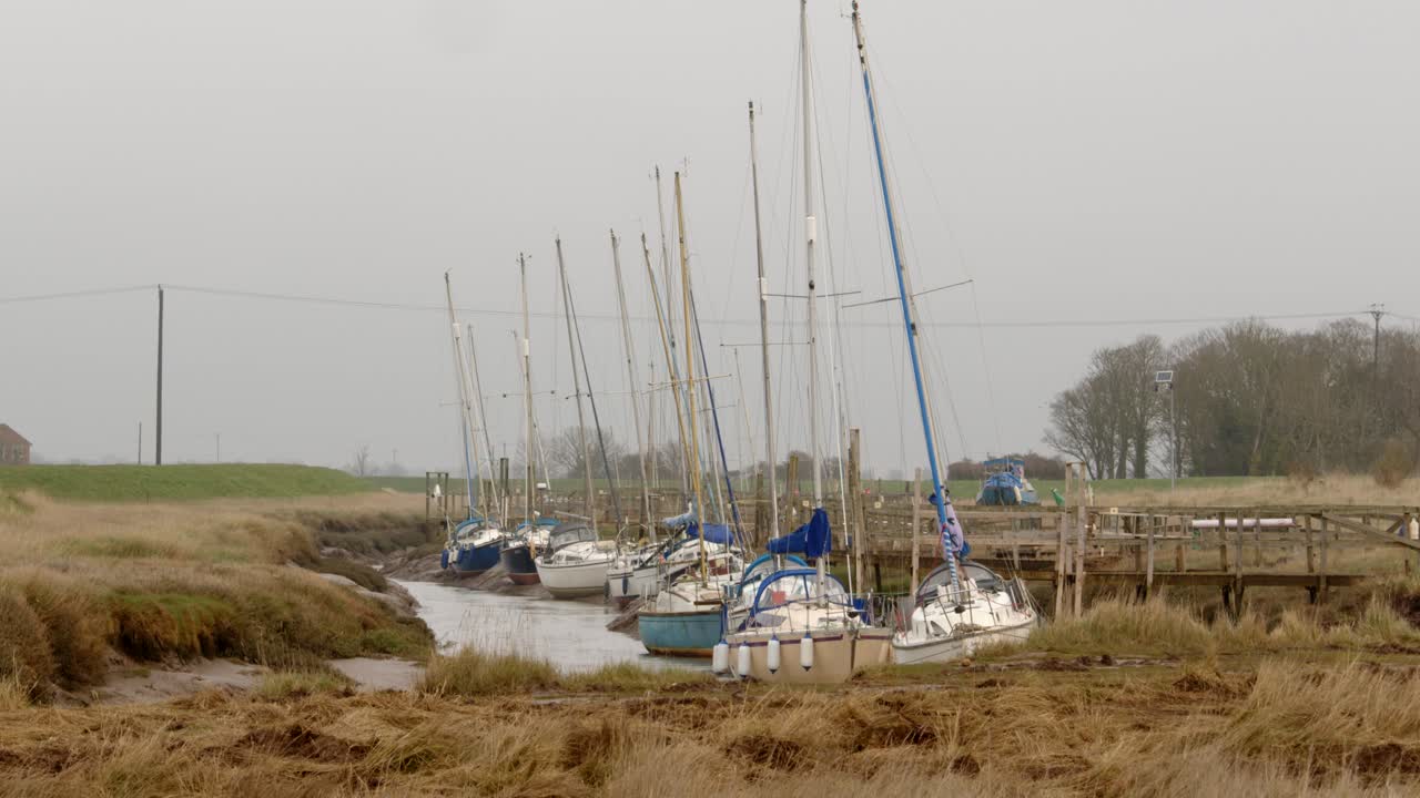 Yachts moored on Steeping River at Gibraltar Point, with the tide out showing mud banks. Extra wide shot
