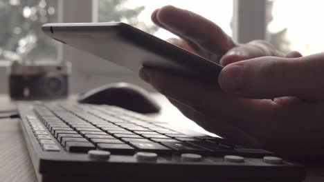 close up on hands of young man using tablet while sitting computer keyboard and mouse. freelancer photographer working and using tablet for communication with clients.