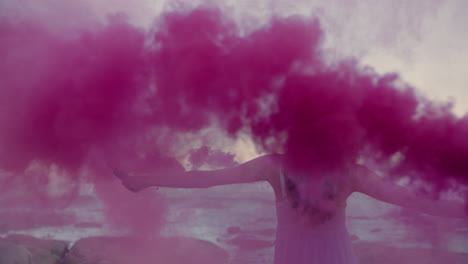 hermosa mujer agitando granada de humo rosa bailando en la playa temprano en la mañana celebrando la libertad creativa