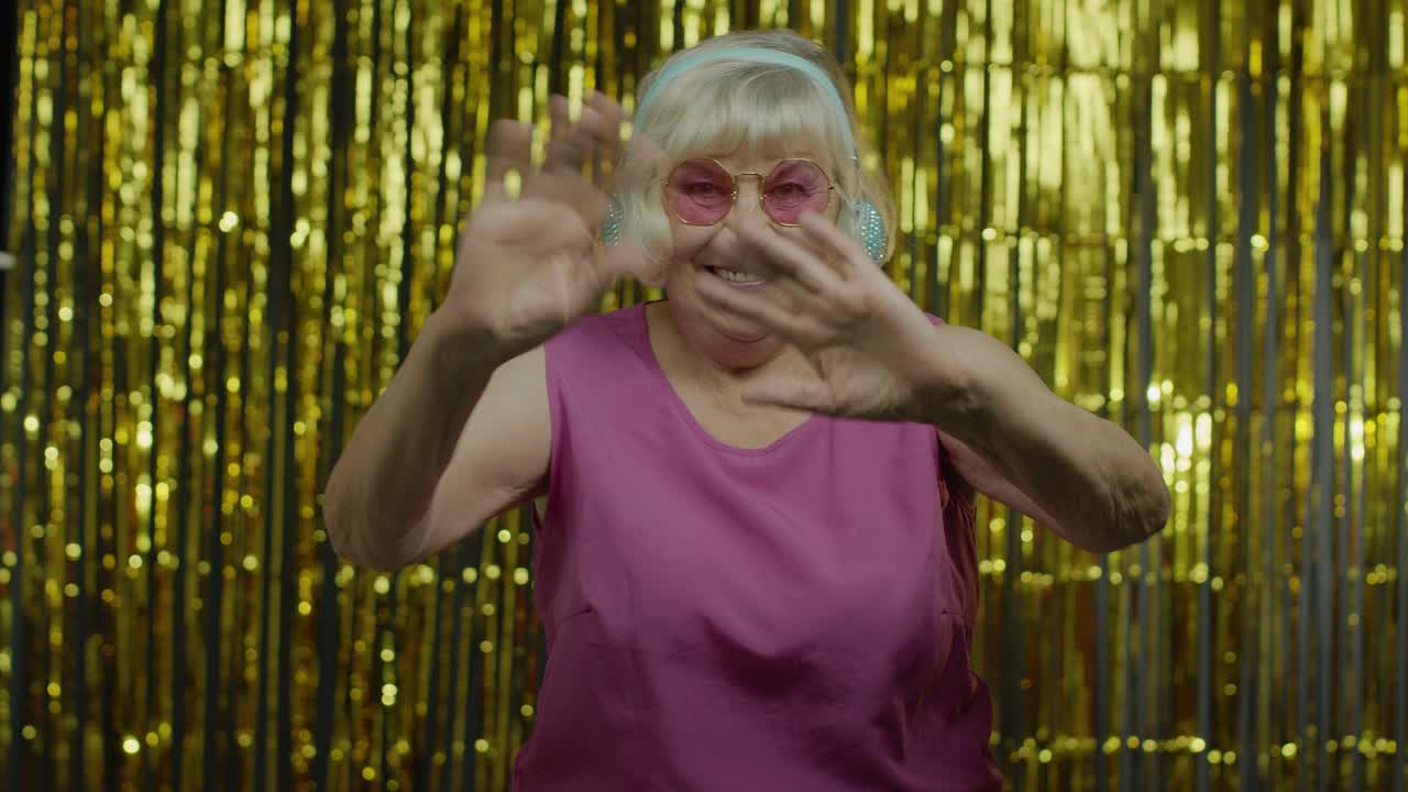 Anziana donna amichevole che saluta con la mano guardando la telecamera con un sorriso smagliante, dicendo ciao, salutando