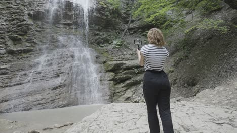 mujer filmando una cascada en un bosque