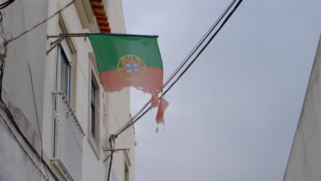 bandera hecha jirones de portugal que sopla en el viento en un callejón en nazare, portugal