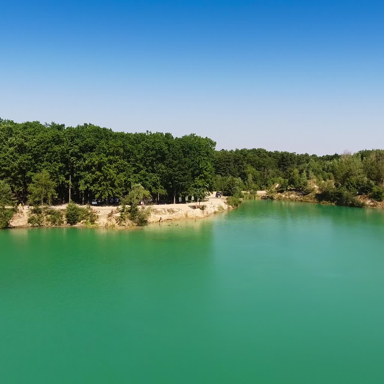 Blue sky reflecting in water. Gradual approaching to the waterfront covered with thick forests. Aerial view