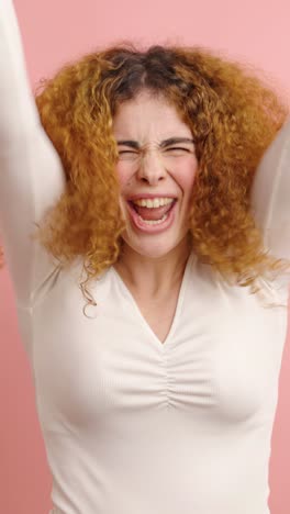 young woman expressing excitement while using smartphone on pink background