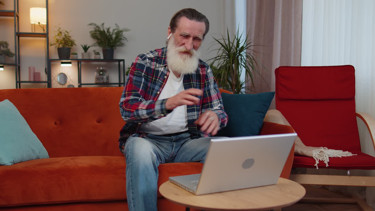 Senior man sitting at home, looking at laptop, making video conference call with friends or family