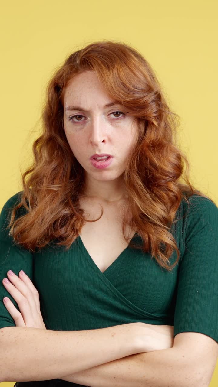 Unhappy Woman with Red Hair and Crossed Arms on Yellow Background