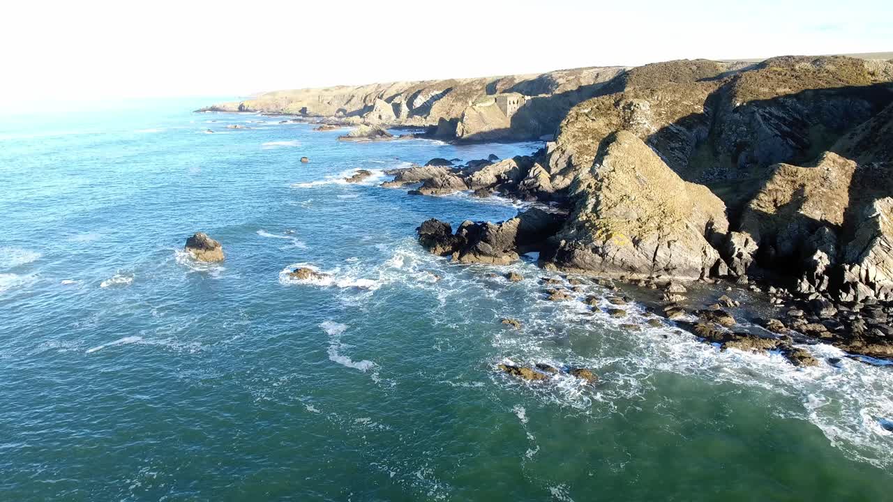 Veduta aerea che segue il profilo di una costa rocciosa di un'isola, con le onde che si infrangono contro il litorale frastagliato.