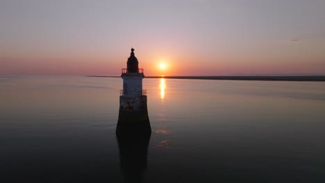 slow approach to abandoned derelict lighthouse in very calm waters with setting sun occluded. plover scar lighthouse, lancashire, uk.