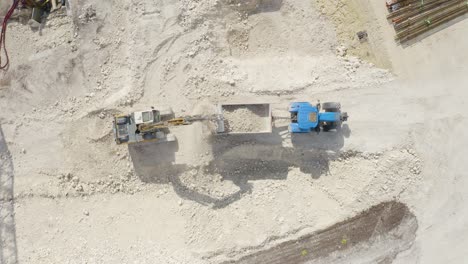 aerial top down shot over a jcb removing soil and putting it on a blue tractor inside a construction site at daytime