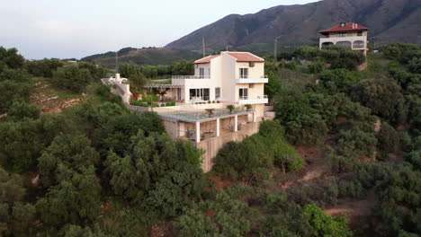 alejamiento aéreo de una lujosa villa griega con piscina con montañas en el fondo y follaje verde en primer plano - coche en marcha