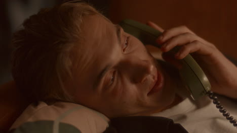 close-up of man resting on pillow, talking on vintage telephone