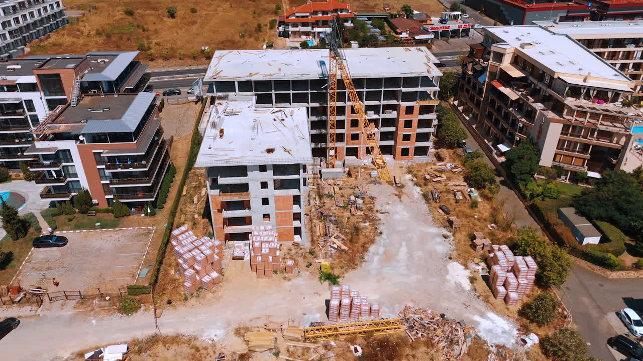 Varna, Bulgaria, 29 June 2025: Construction scene with stacked materials and crane. Building frames rise above pallets of bricks and construction debris in a dusty environment