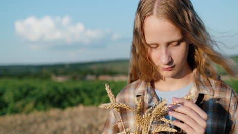 Portrait-of-a-teenage-girl-with-spikelets-of-wheat-in-her-hand.-Stands-against-the-backdrop-of-picturesque-countryside-and-wheat-fields