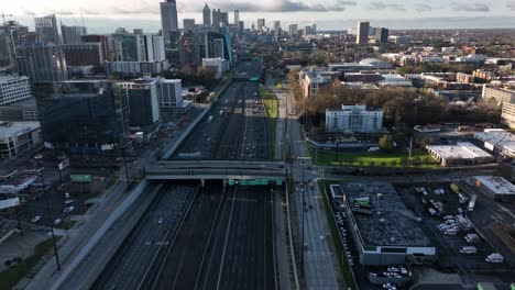 a cinematic drone shot reveals moving traffic on downtown atlanta interstate highway with the view of famous skyscrapers in the background at sunset