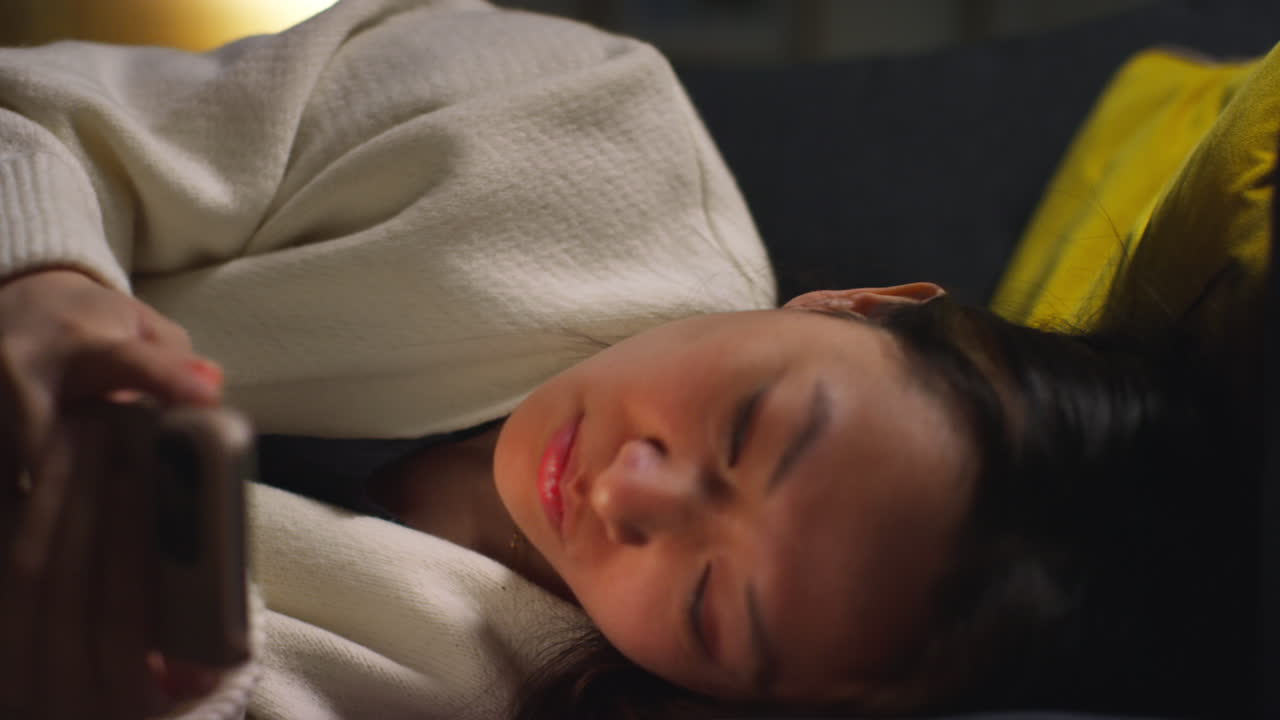 집에서 저녁을 보내고 소파에 누워서 인터넷이나 소셜 미디어를 스크롤하는 여성의 클로즈업