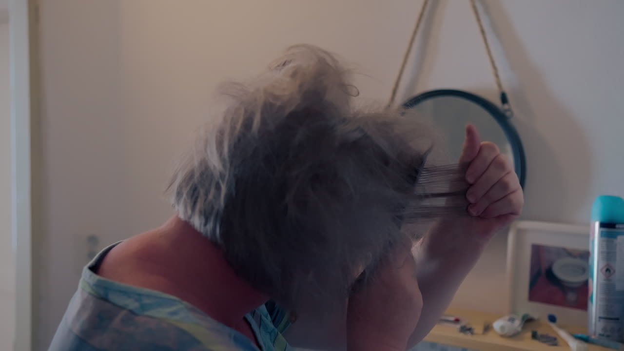 Older fat woman styling her hair, creating volume with a comb in front of the small circle mirror inside the bathroom
