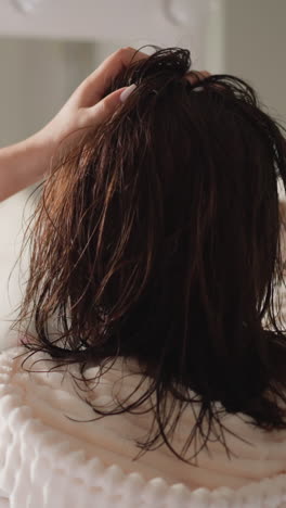 en túnica femenina gira el cabello húmedo volando en el baño iluminado en cámara lenta. la mujer mueve las manos ajustando el cabello en el baño con reflejo borroso en el espejo