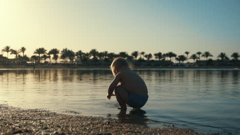 lovely child playing in seawater at sunset coastline. toddler playing with toy.
